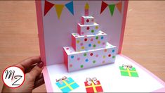 a hand is holding up a card that has a birthday cake and presents on it