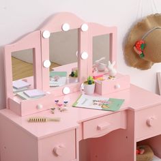 a child's pink vanity with mirror, lights and toys on it in a room