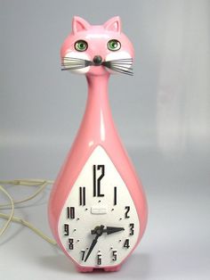 a pink clock with a cat's face on it and green eyes is sitting in front of a gray background