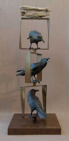 three metal birds sitting on top of each other in front of a white wall and brown base