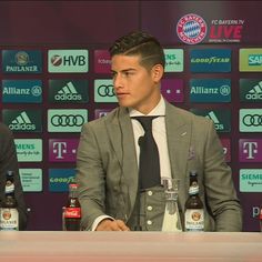 two men sitting next to each other in front of a wall with soccer logos on it