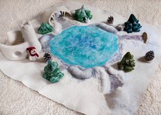 a table topped with miniature trees and snow covered rocks on top of a white blanket