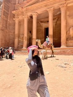 a woman standing in front of a building with two camels on the other side