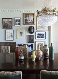 a dining room table with vases and pictures on the wall above it in front of a chandelier