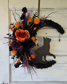 a wreath with an orange flower and black cat decoration on the front door to a house