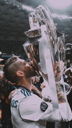 a man holding up a trophy in front of a crowd at a sporting event and kissing it