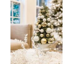 a small christmas tree sitting on top of a pile of white and gold ornaments in a living room