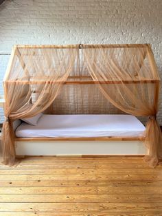 a bed with mosquito netting over it on top of a wooden floor next to a brick wall