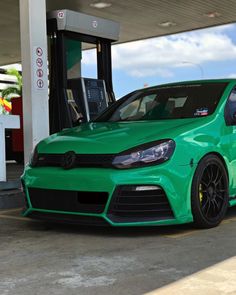 a green vw golf gtr is parked in front of a gas station with its door open