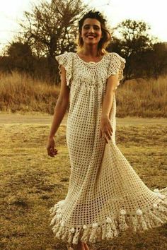 a woman in a white crochet dress is standing on the grass and smiling