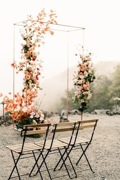 two wooden benches sitting next to each other on a gravel field with flowers growing over them