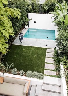 a small pool in the middle of a garden with grass and plants around it, surrounded by greenery