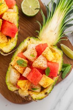 two pineapples with slices of watermelon and mint on them, sitting on a cutting board