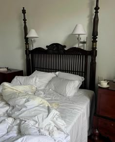 an unmade bed with white sheets and two lamps on either side of the headboard