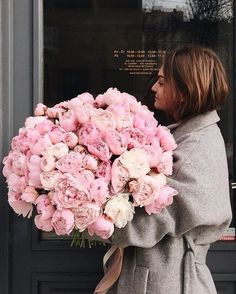 a woman holding a large bouquet of pink peonies in front of a door