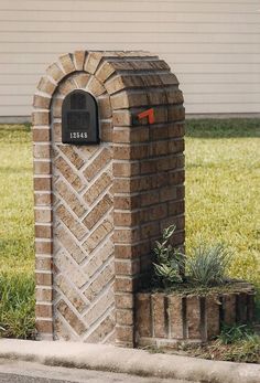 a brick mailbox sitting on the side of a road next to a grass field