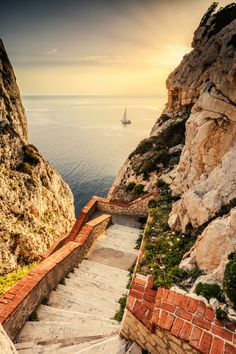 stairs leading up to the top of a cliff overlooking the ocean with a sailboat in the distance