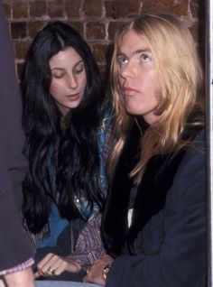 two women sitting next to each other in front of a brick wall and looking at something