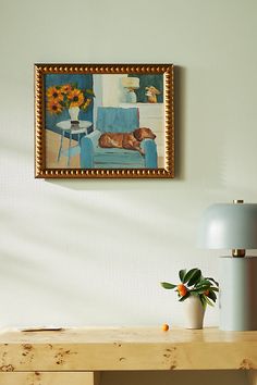 a painting hangs on the wall next to a table with a vase and plant in it