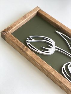 a wooden frame with metal utensils in it on top of a white table