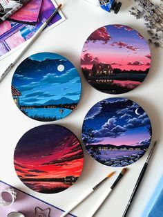 four circular coasters are sitting on a table next to paint brushes and pencils