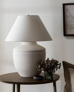 a white vase sitting on top of a wooden table next to a lamp and flowers