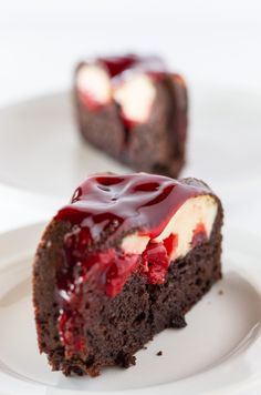 a piece of chocolate cake with raspberry topping on a white plate next to another slice