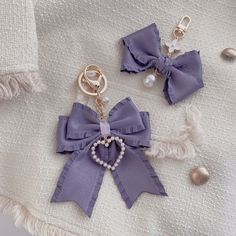 two key chains with bows and pearls attached to them on a white blanket next to beads