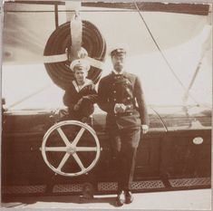 two men standing next to each other in front of a sail boat with a cross on it