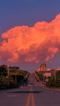 the sky is pink and orange as cars drive down the road in front of some clouds