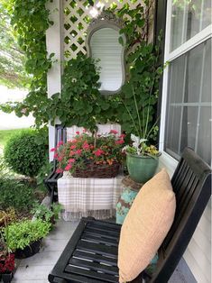 a black bench sitting on top of a porch next to potted plants and flowers