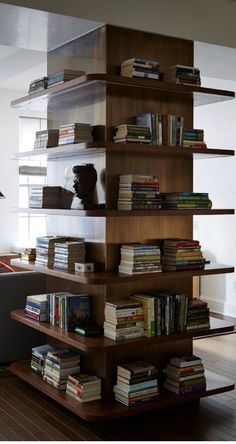 a living room filled with lots of books on top of wooden shelves next to a gray couch