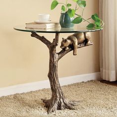 a glass table topped with a bear on top of a tree branch next to a potted plant