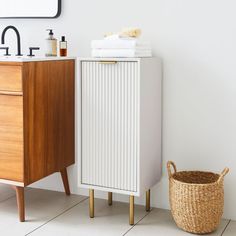 a white cabinet sitting next to a bathroom sink and wooden dresser with towels on top