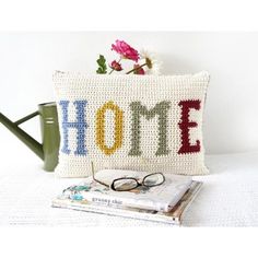 a crocheted pillow with the word home on it next to a watering can