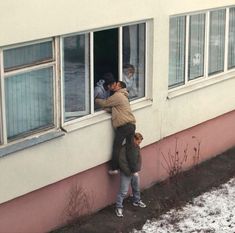 two men are standing on the side of a building and one man is leaning against the window