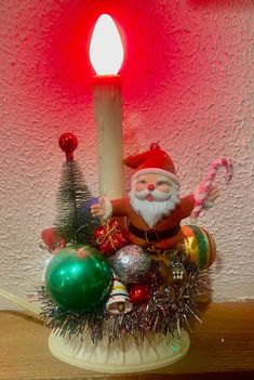 a lit candle sitting on top of a table next to christmas decorations and ornaments in front of a red wall