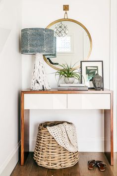 a small white table with a basket on it and a round mirror above the table