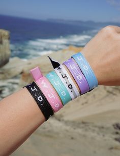 a person wearing bracelets on their wrist next to the ocean and rocks in the background