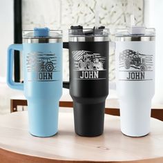 three travel mugs sitting on top of a wooden table next to each other with the words john written on them