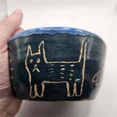 a hand holding a black and gold painted ceramic object with a dog on it's side