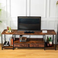 a flat screen tv sitting on top of a wooden table next to a plant and books