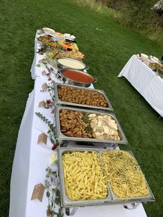 a long table with many trays of food on it and two tables covered in white cloths