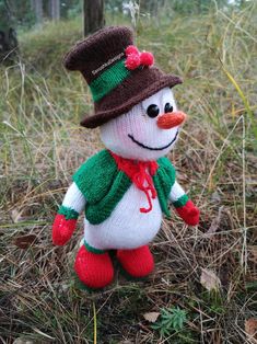 a small knitted snowman in a green scarf and hat standing on the ground