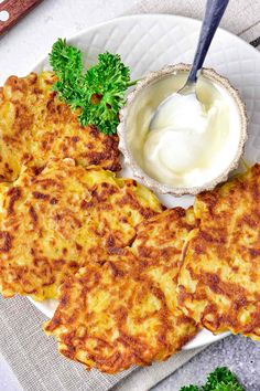 some food on a white plate with a bowl of yogurt and parsley