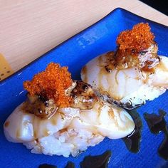 two pieces of fish on a blue plate covered in sauce and garnishes