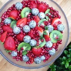 a bowl filled with fruit and berries on top of a wooden table next to green plants