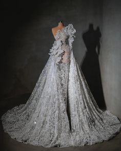 the back of a wedding dress on display in a dark room with a mannequin standing next to it