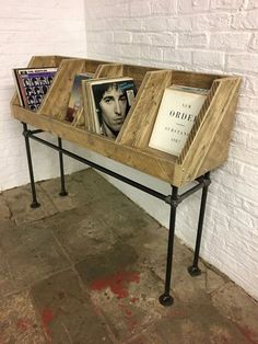 a wooden table with two magazine racks on it and books in the bottom shelf, against a white brick wall