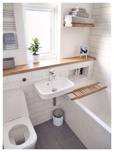 a small bathroom with white tile and wood shelves above the toilet, sink, and bathtub